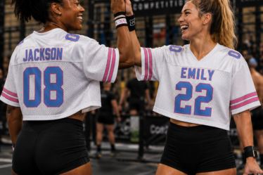 Two female CrossFit athletes celebrating with a high five during a fitness competition while wearing personalised sports jerseys.