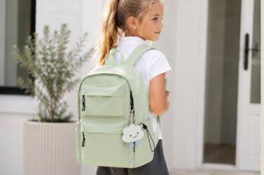 Young schoolgirl wearing a mint green backpack with a cute cloud keychain, dressed in uniform ready for the first day of school.