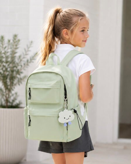 Young schoolgirl wearing a mint green backpack with a cute cloud keychain, dressed in uniform ready for the first day of school.