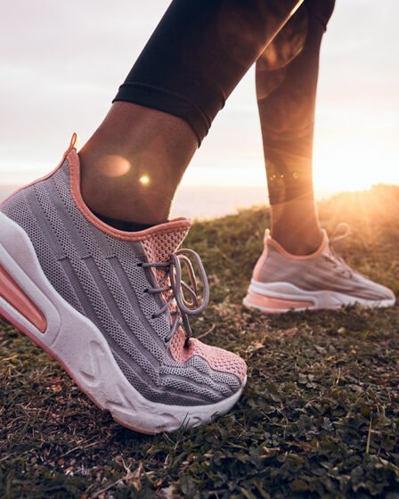 Woman wearing pink running shoes on a coastal trail at sunrise, highlighting cushioned trainers designed for comfort and everyday running.