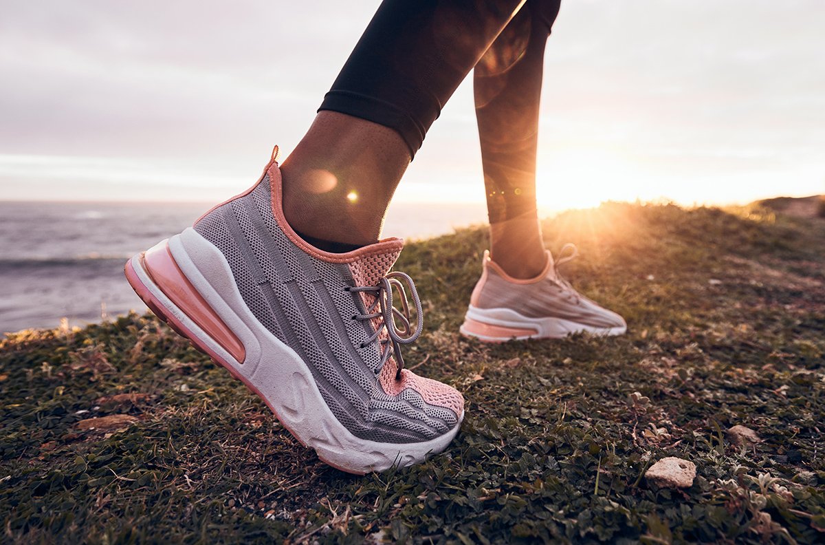 Woman wearing pink running shoes on a coastal trail at sunrise, highlighting cushioned trainers designed for comfort and everyday running.