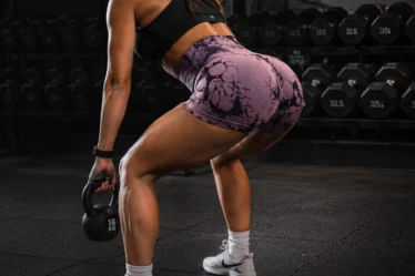 Athletic woman performing a kettlebell squat in a modern gym while wearing patterned scrunch bum gym shorts and a black sports bra.
